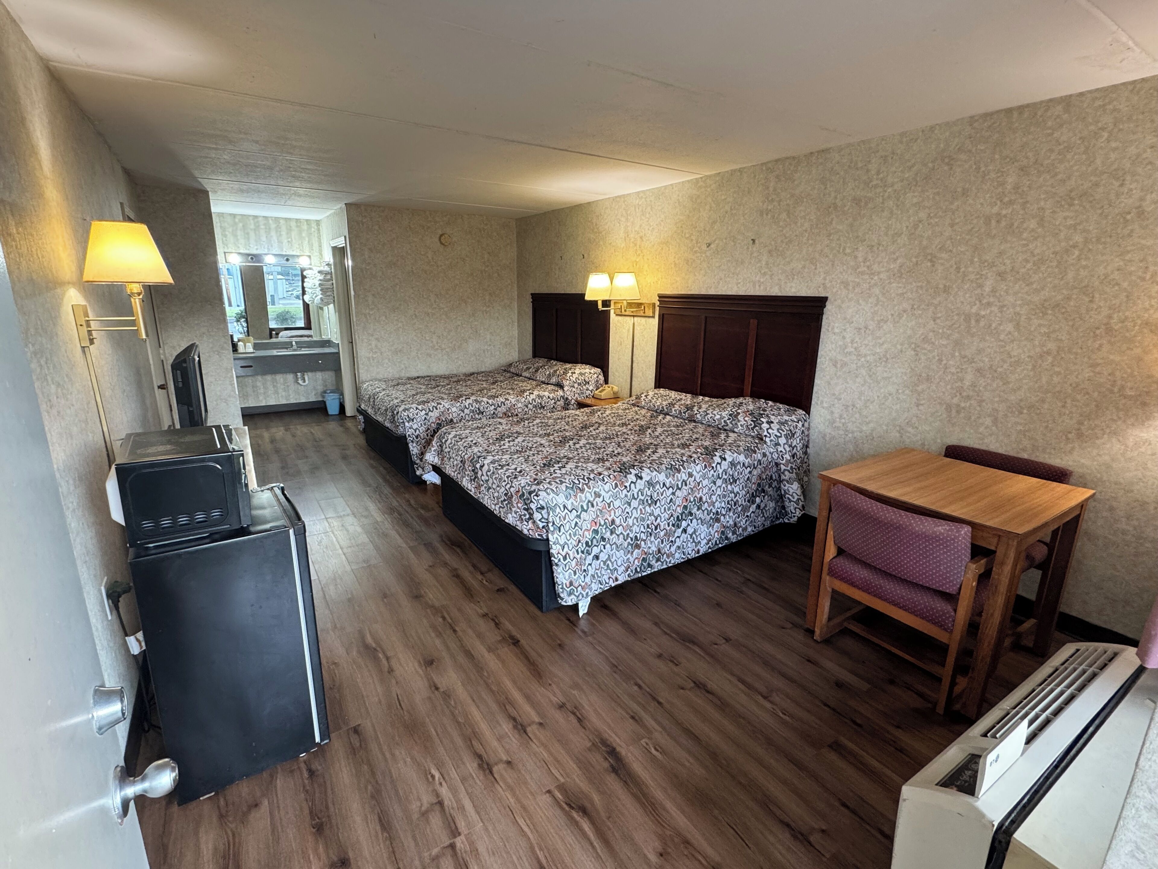 Hotellihuone, jossa on sänky, yöpöytälamput, työpöytä, tuoli, mikroaaltouuni ja lämmitin.