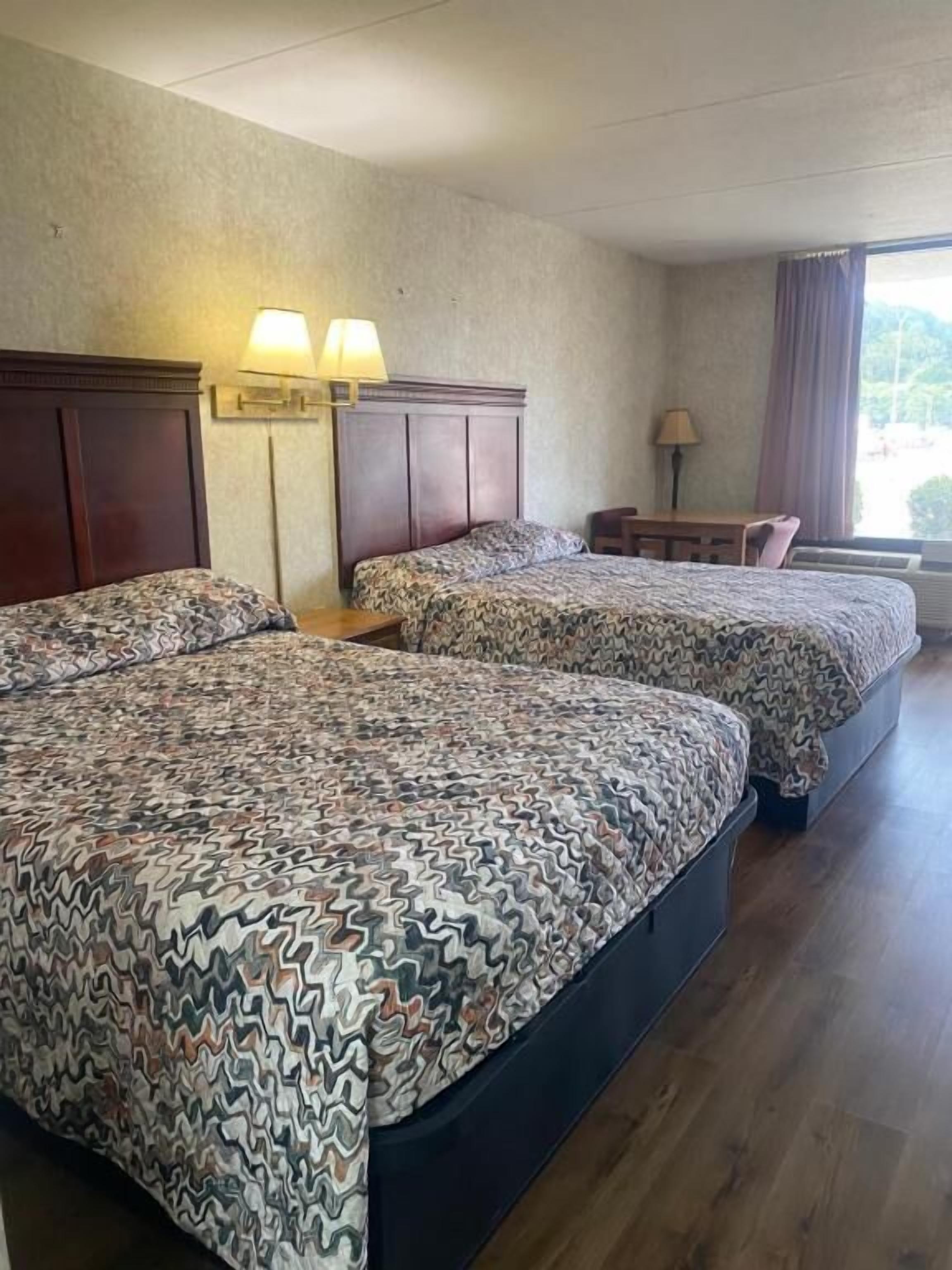A hotel room with two beds, a desk, and a window.
