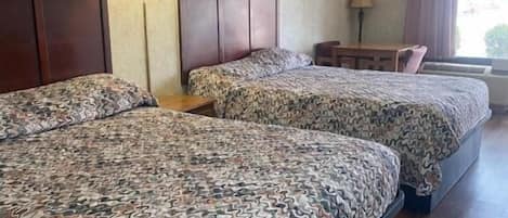 A hotel room with two beds, a desk, and a window.