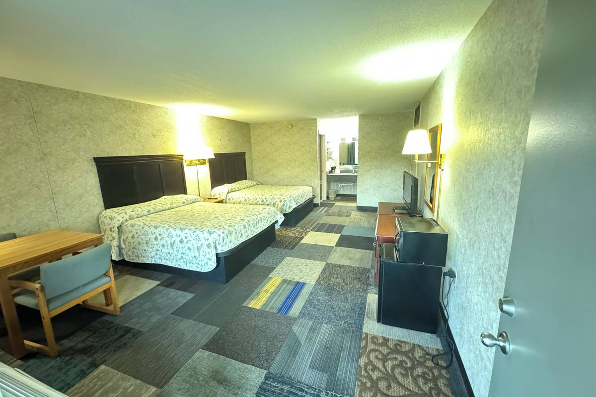 A hotel room with two beds, a desk, a TV, and a bathroom visible through an open door.
