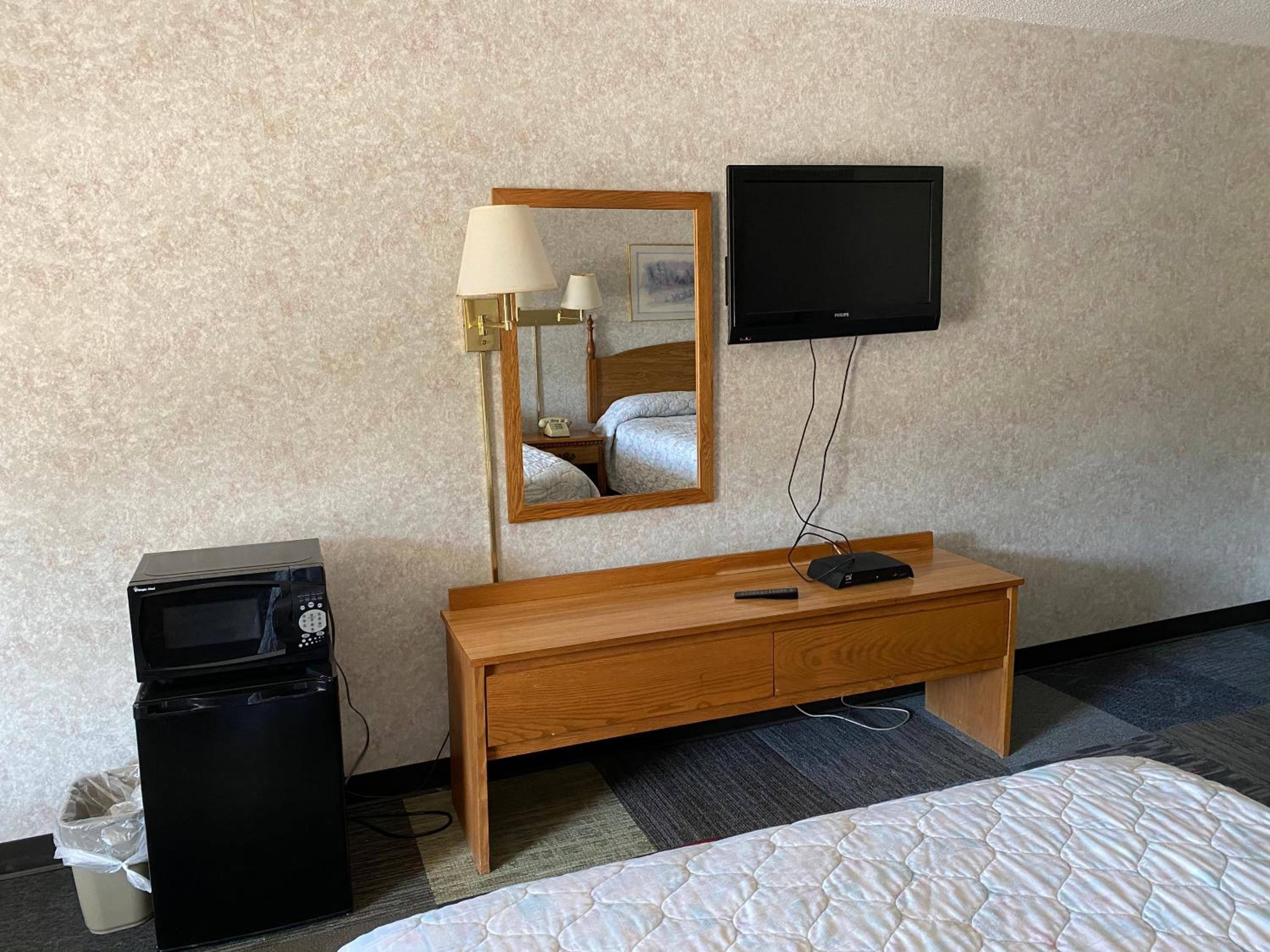 Ett hotellrum med en säng, ett träbord vid sängen med en lampa, en tv som är monterad på väggen och en liten svart värmare.