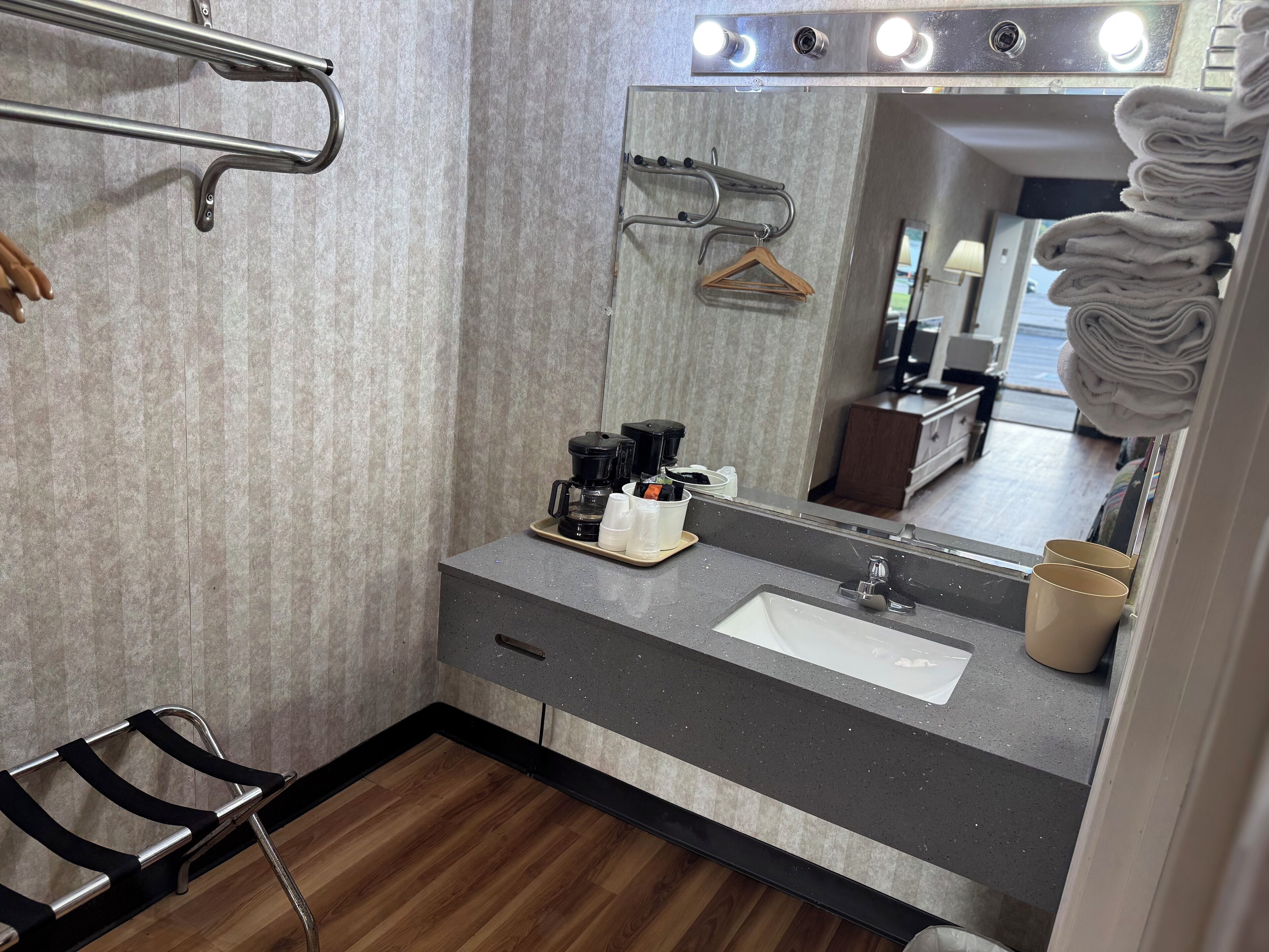 A bathroom with a vanity, sink, mirror, towel rack, and a shower chair.