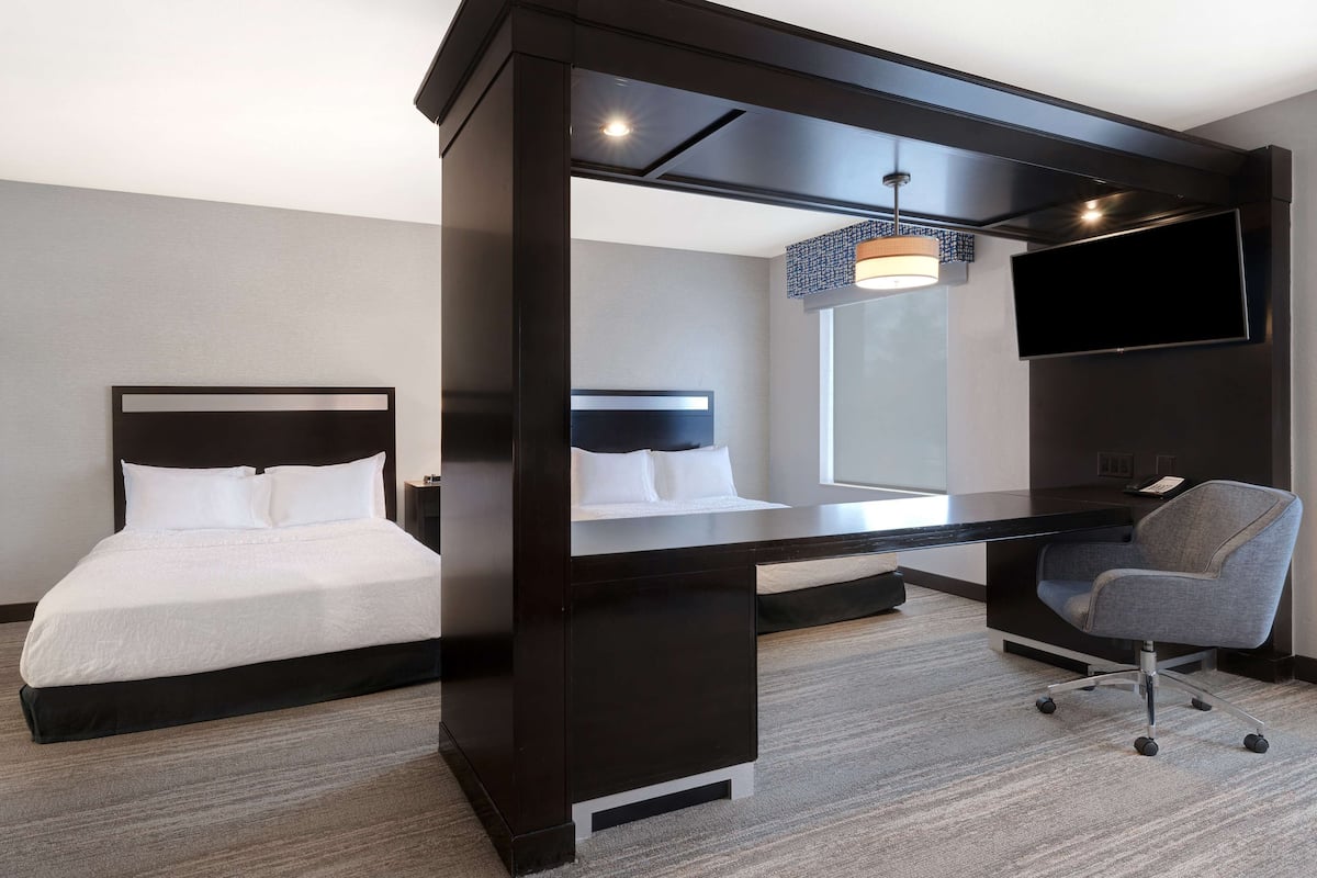 A hotel room with a bed, a desk, a chair, and a TV mounted on the wall.