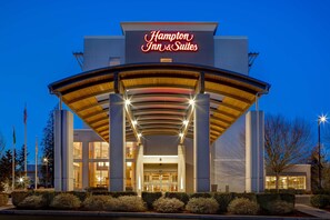A Hampton Inn & Suites hotel entrance with a modern design, featuring a prominent sign, a covered entrance, and well-maintained landscaping.