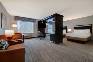 A hotel room with a bed, a desk, a chair, and a sofa.