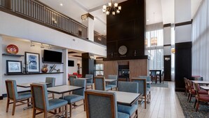 A hotel lobby with multiple dining tables and chairs, a fireplace, artwork on the walls, and a staircase leading to an upper level. - Hampton Inn & Suites Seattle/Federal Way (Federal Way)