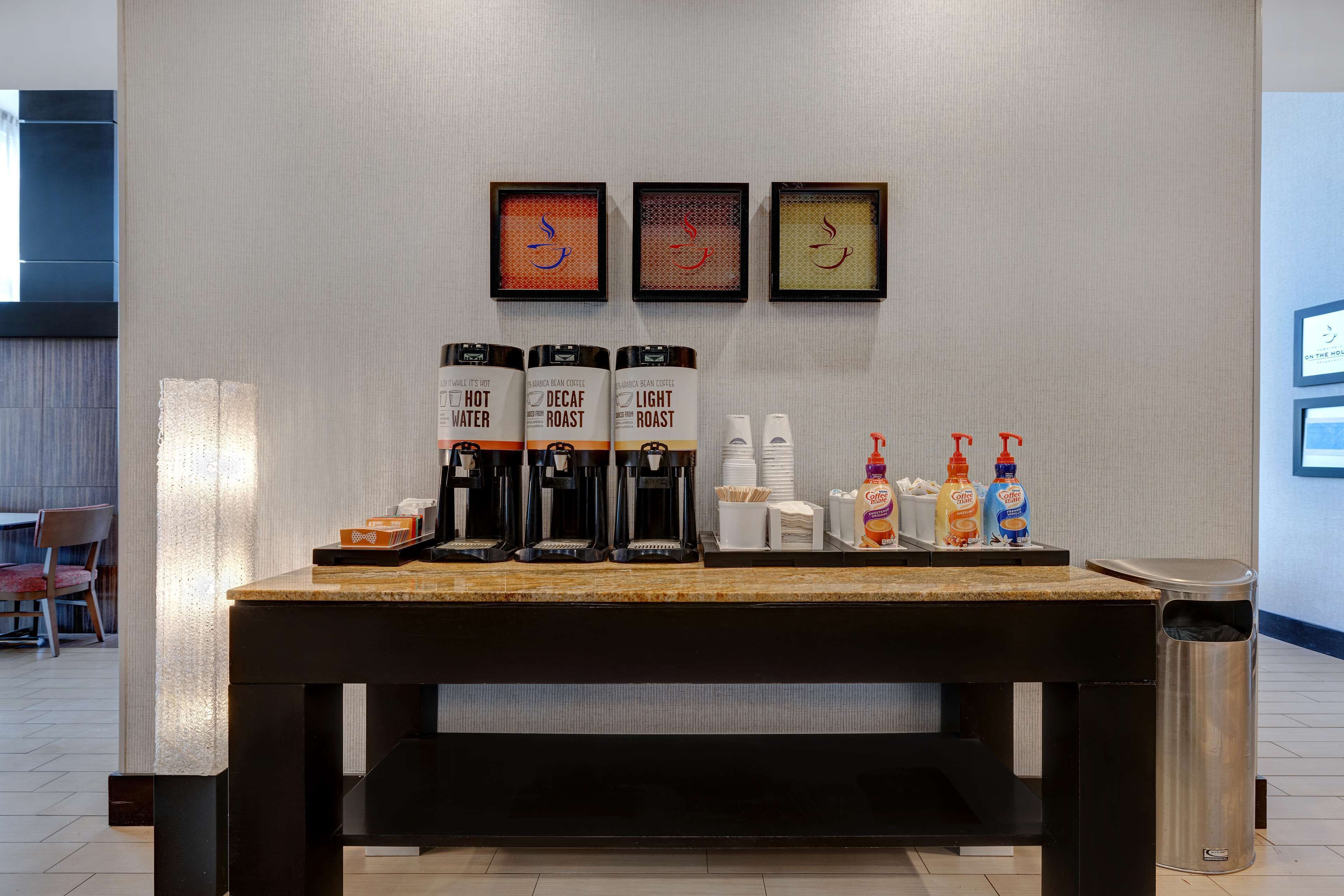 Una estación de café con opciones descafeinado y tostado claro, vasos desechables y condimentos.