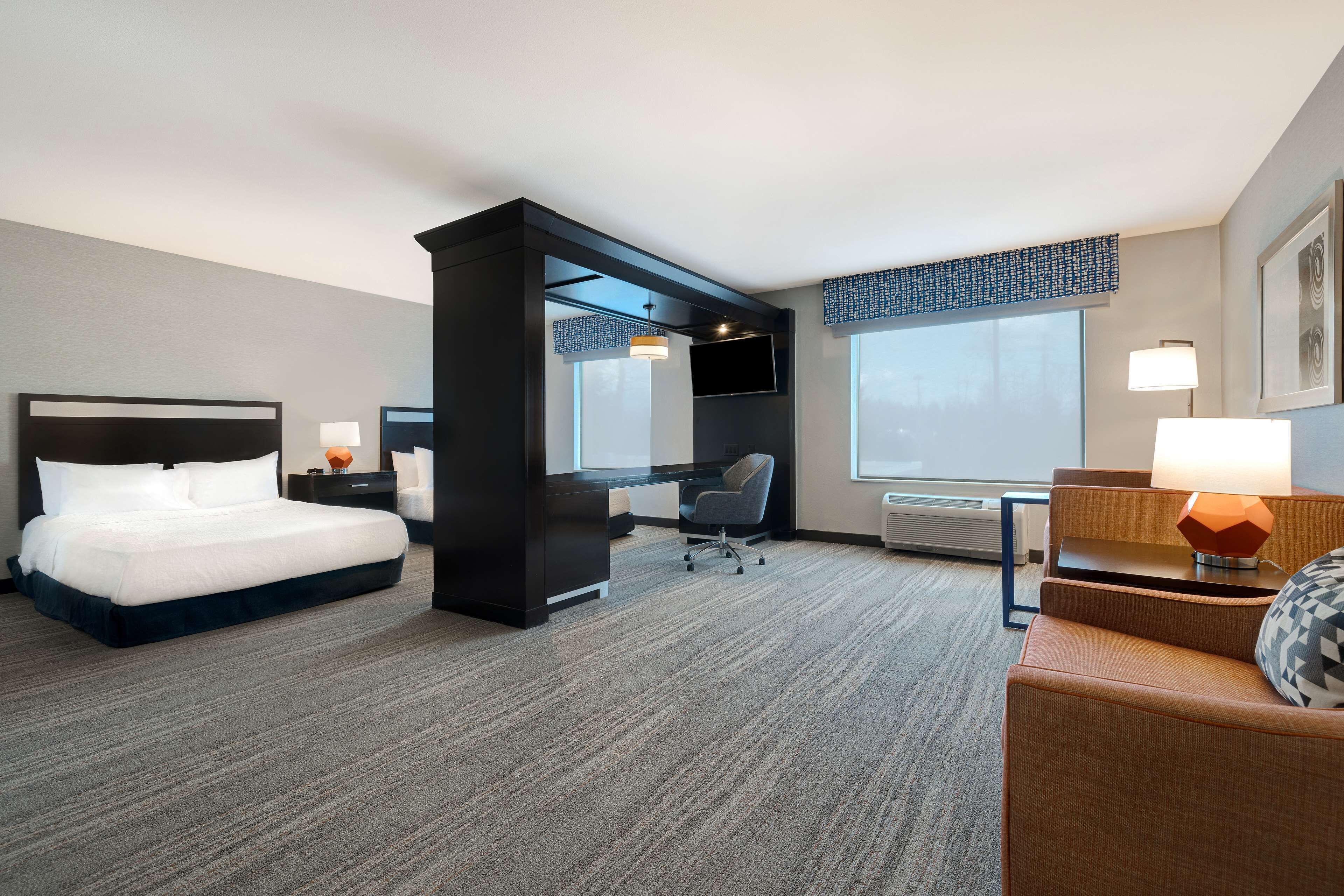 Ein Hotelzimmer mit Bett, Schreibtisch, Stuhl und großen Fenstern.