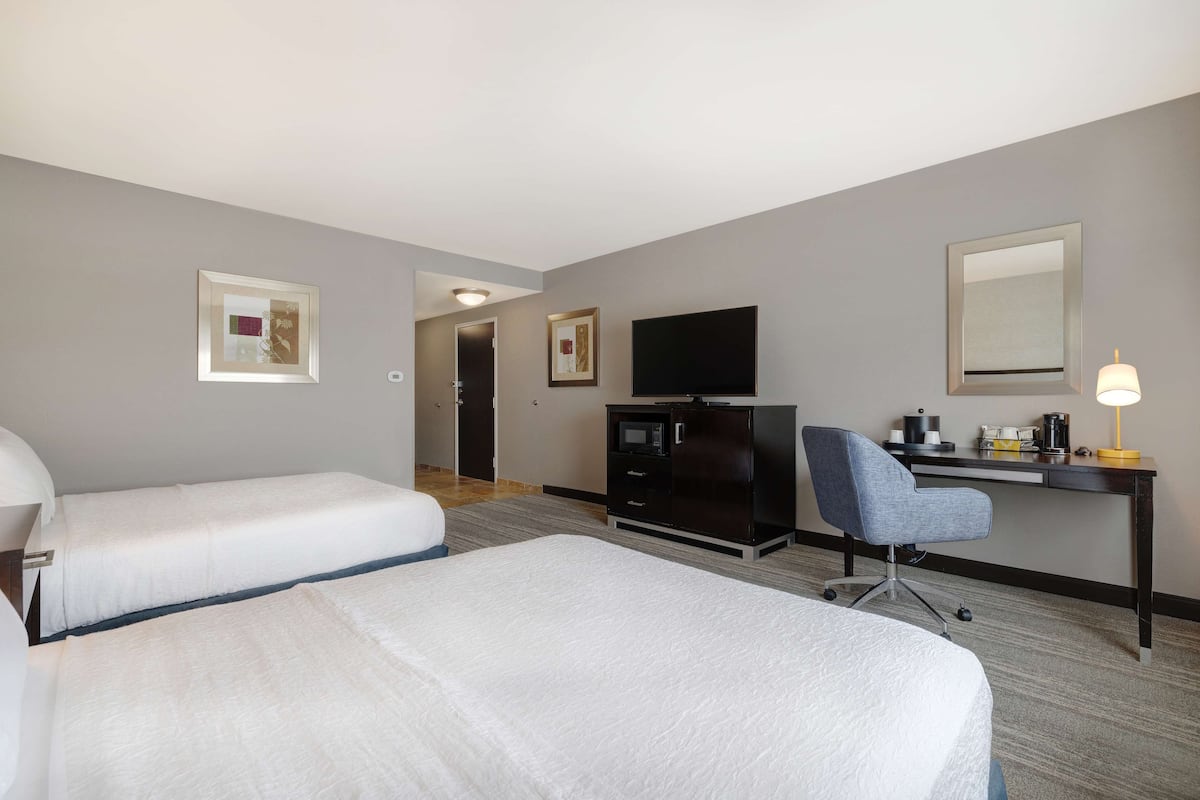 A hotel room with two beds, a desk with a computer, a TV, and a lamp.