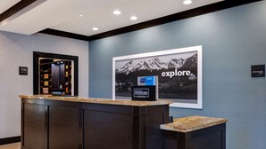 A hotel reception desk with a framed 'explore' sign and a 'Hilton Honors' sign. - Hampton Inn & Suites Seattle/Federal Way (Federal Way)