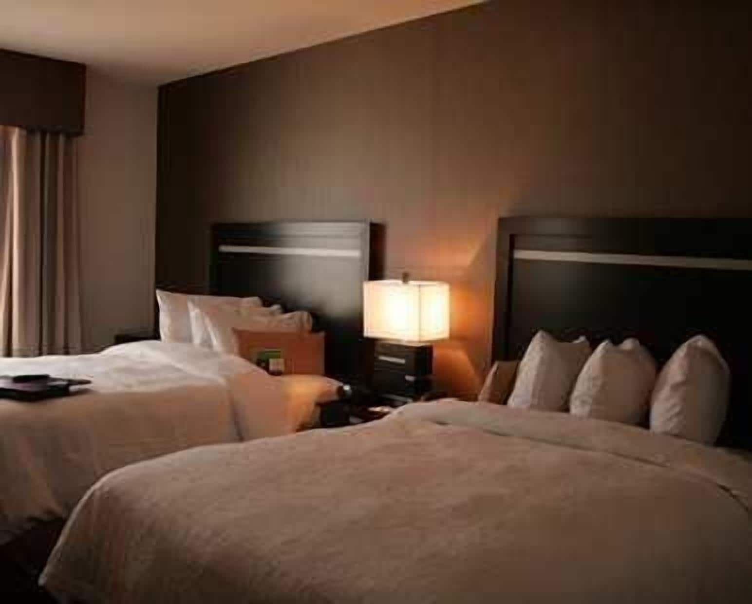 A hotel room with two beds, a nightstand with a lamp, and a window with curtains.