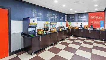 Un área de desayuno con piso a cuadros, una estación de waffles e ilustraciones de comida en una pared.