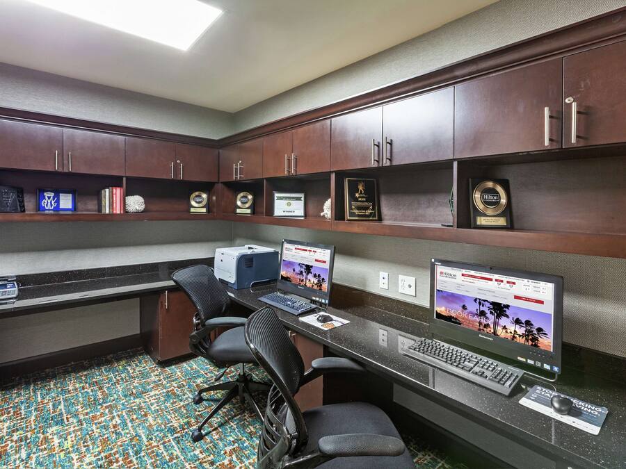 A hotel room with a desk, two laptops, a printer, and a carpeted floor.
