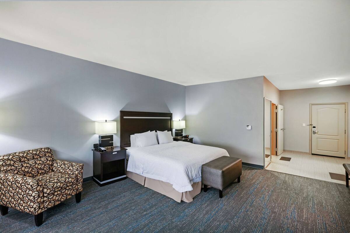 A hotel room with a bed, bedside tables, a chair, a bench, and a door.