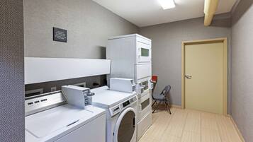 Un cuarto de lavado con lavadora y secadora de carga frontal, una silla pequeña y una puerta.