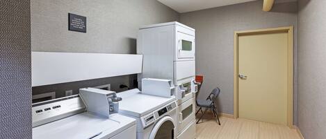 A laundry room with a front-loading washer and dryer, a small chair, and a door.
