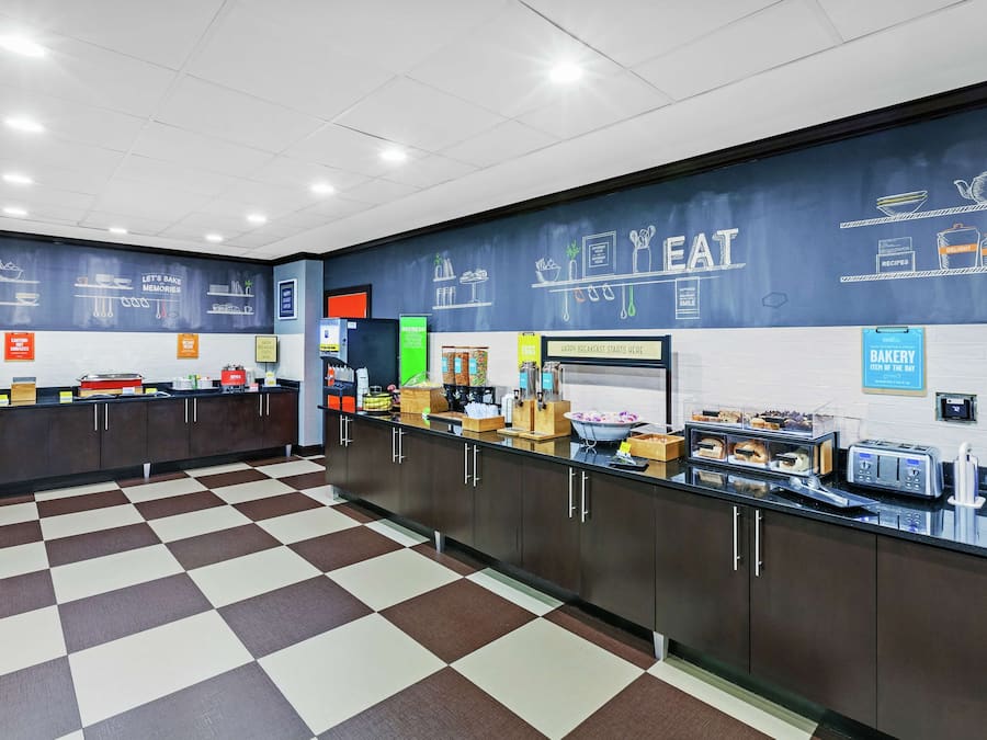 A breakfast area with a checkered floor, a counter with various food items, and a wall with kitchen utensils and food-related drawings.
