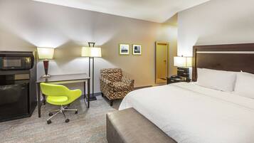 Quarto de hotel com cama, escrivaninha com computador, micro-ondas, cadeira e abajur.