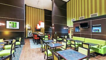 A hotel lobby with green seating, tables, and a TV mounted on the wall.