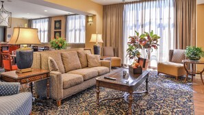 A spacious living room with a sofa, armchairs, a coffee table, and a TV. There are potted plants and a patterned rug. - Hampton Inn Jackson (Jackson)
