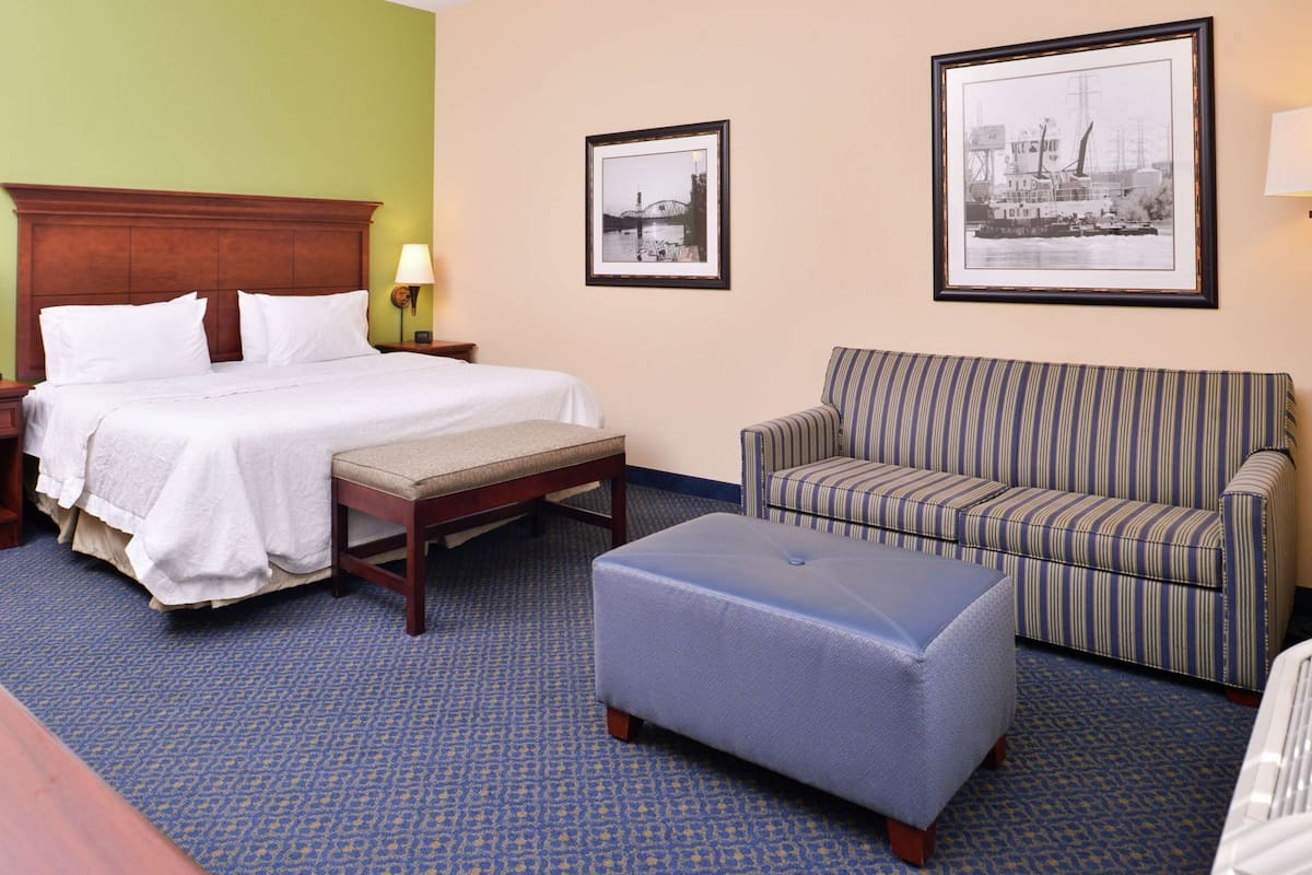 A hotel room with a bed, a bench, a sofa, and two framed pictures on the wall.