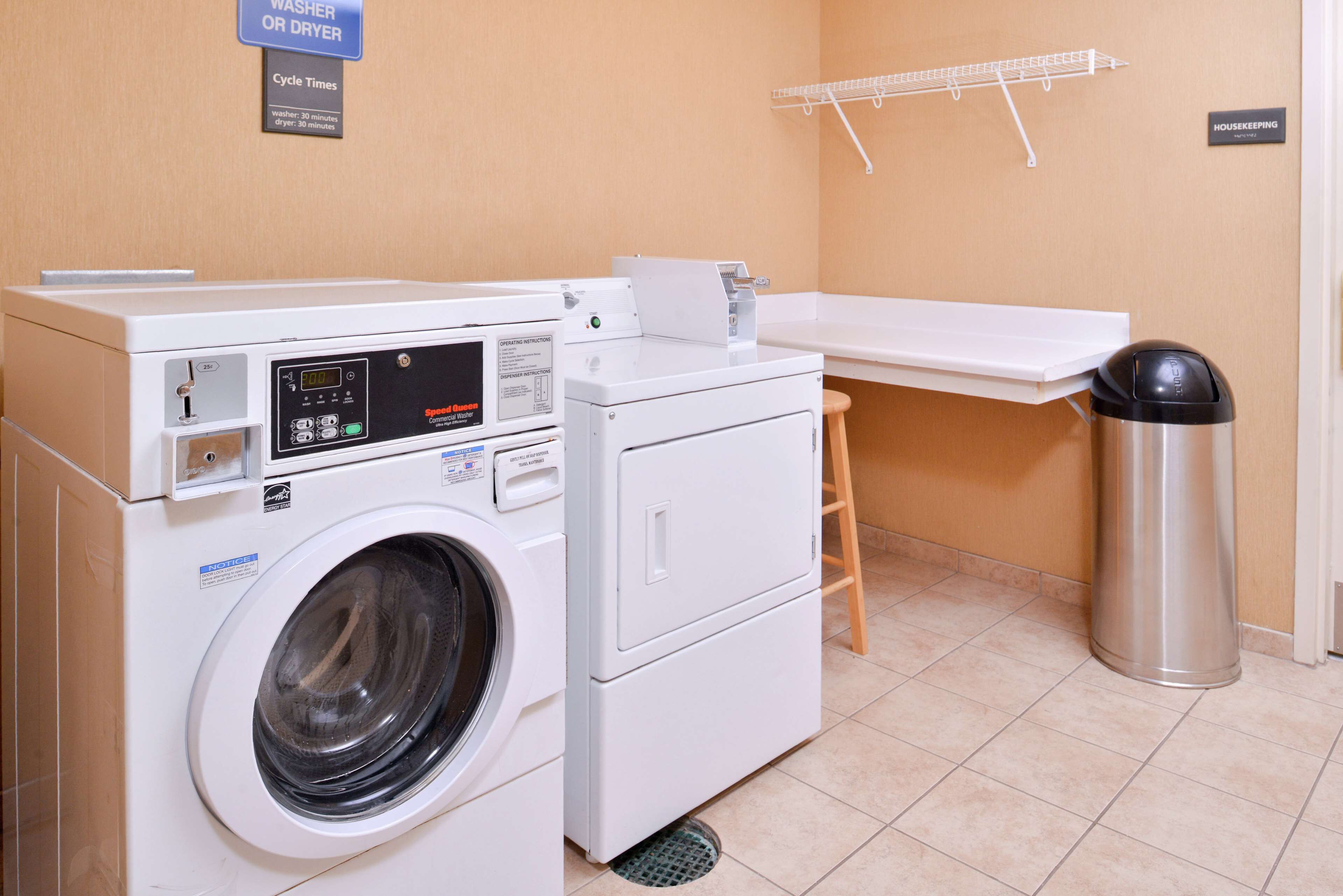 A laundry area with a washing machine, dryer, and a metal trash can.