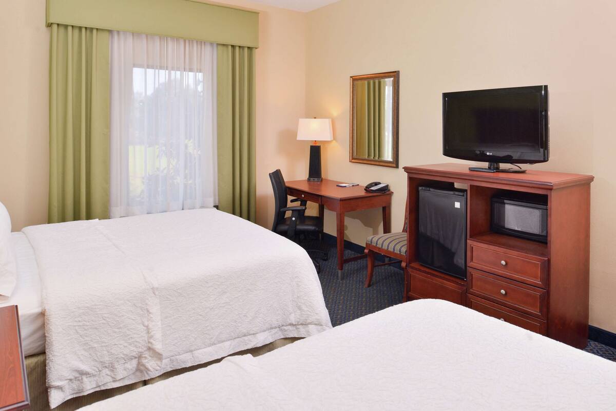 A hotel room with two beds, a desk with a lamp, a television, and a mirror.