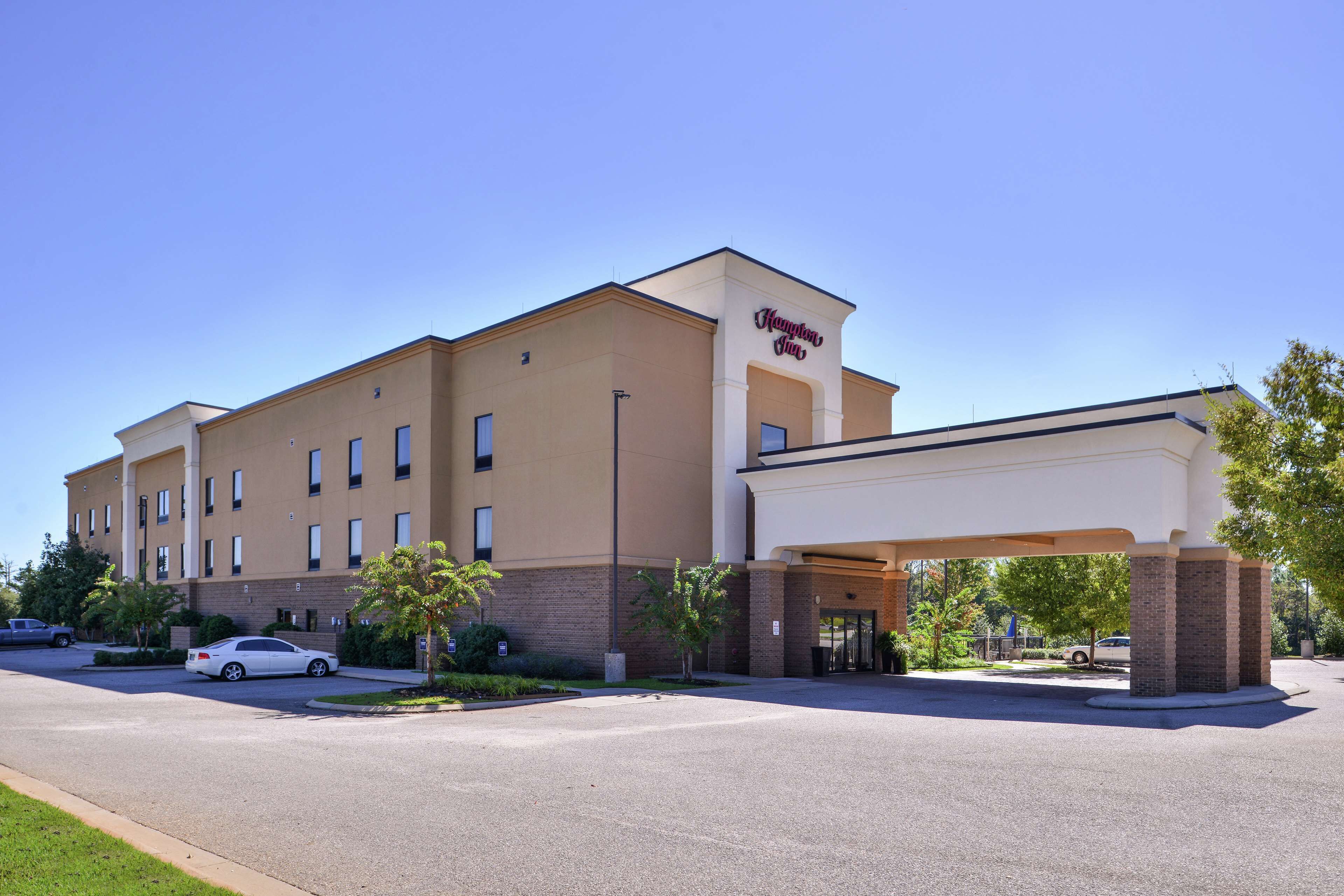A Hampton Inn hotel with a modern design, featuring a prominent entrance and a parking lot.