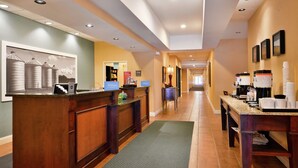 A hotel reception area with a wooden reception desk, a green mat, and a hallway leading to a door. - Hampton Inn Jackson (Jackson)