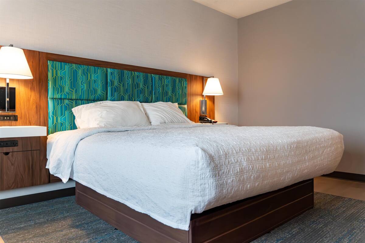 A hotel room with a large bed, wooden headboard, bedside lamps, and a nightstand with a phone.