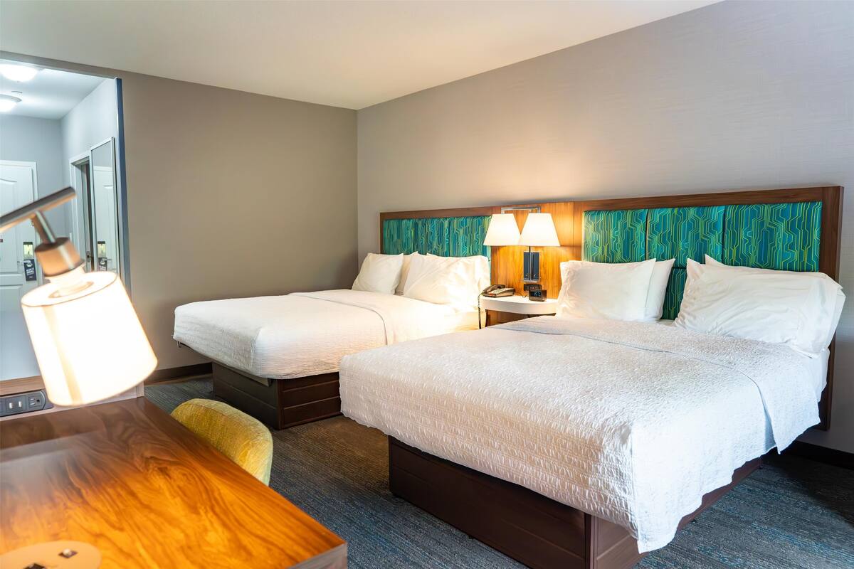 A hotel room with two single beds, a wooden desk, a lamp, and a mirror.