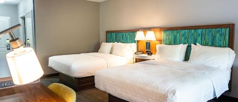 A hotel room with two single beds, a wooden desk, a lamp, and a mirror.