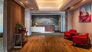 A reception area with a wooden floor, a reception desk, red chairs, and a welcome sign.