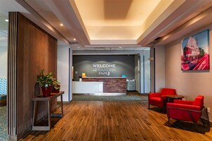 Zona de recepción de un hotel con piso de madera, mostrador de recepción y sillas rojas.