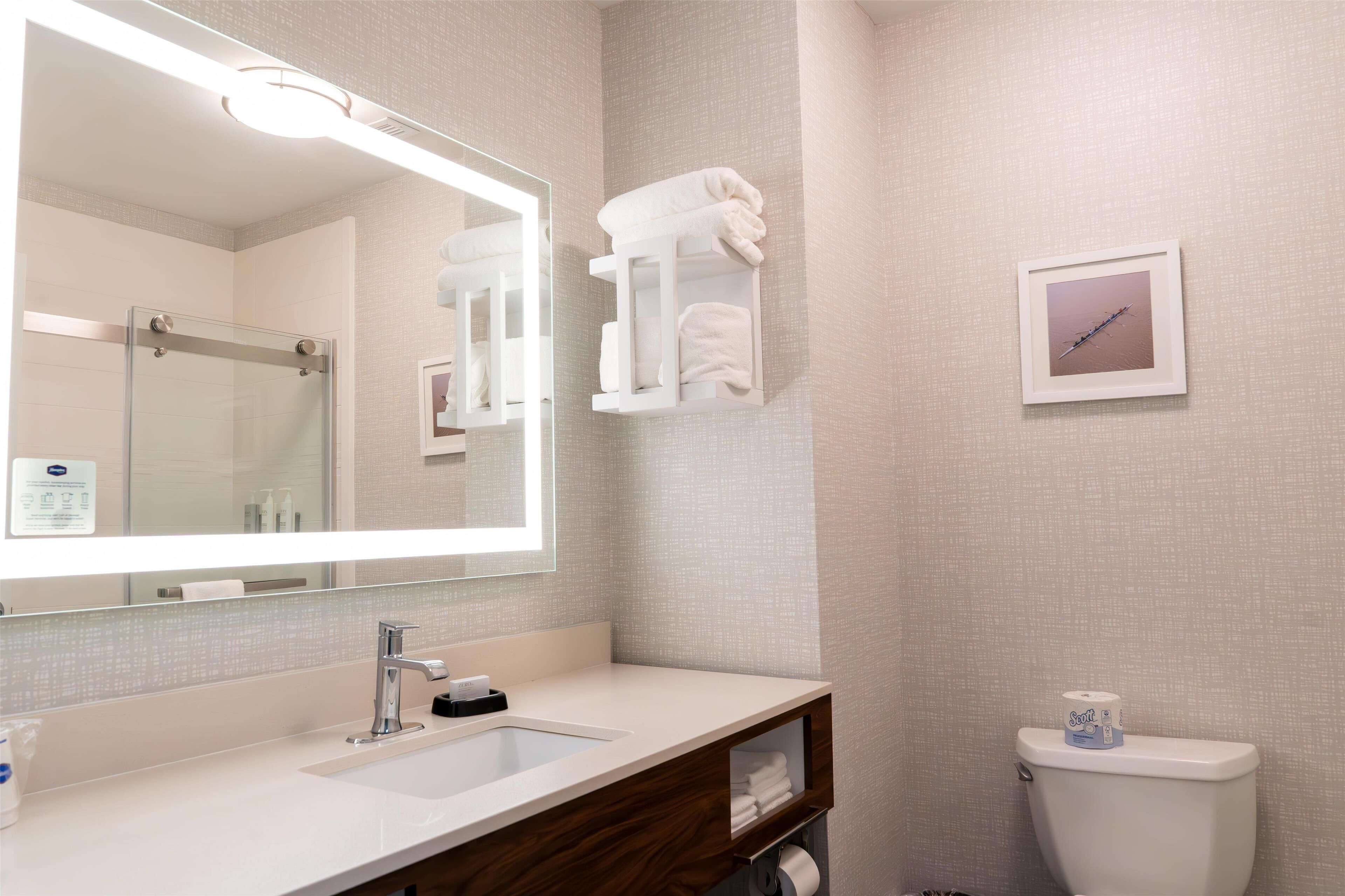 Un baño moderno con un espejo grande, un lavamanos, un inodoro y un perchero para toallas.