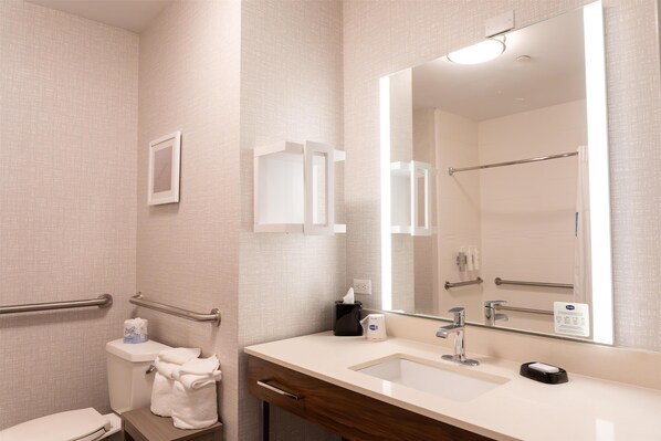 A bathroom with a toilet, sink, mirror, towel rack, and handrails.