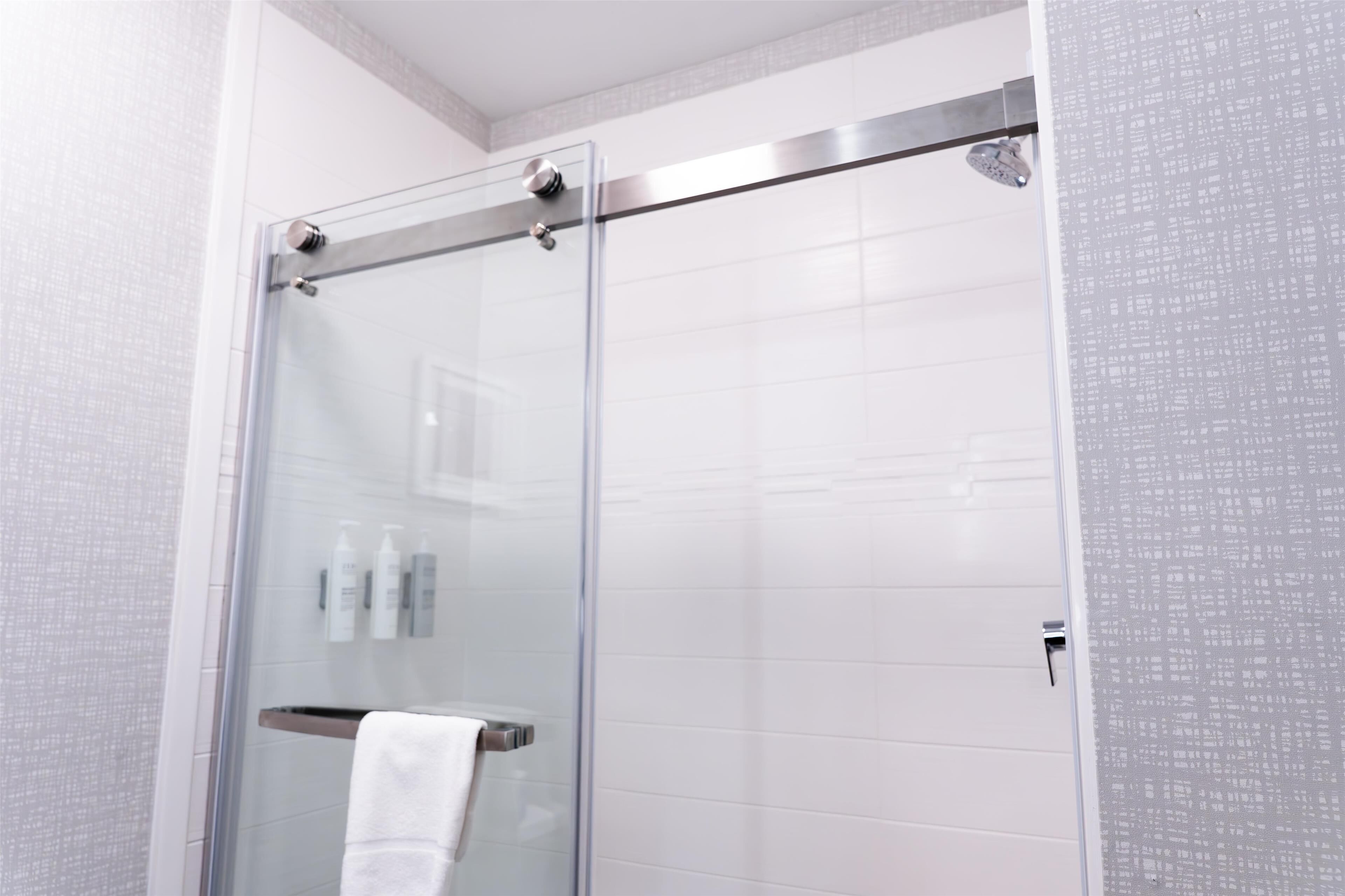 Ein modernes Badezimmer mit einer Duschkabine aus Glas, weißen Fliesen und einem sichtbaren Handtuchhalter.