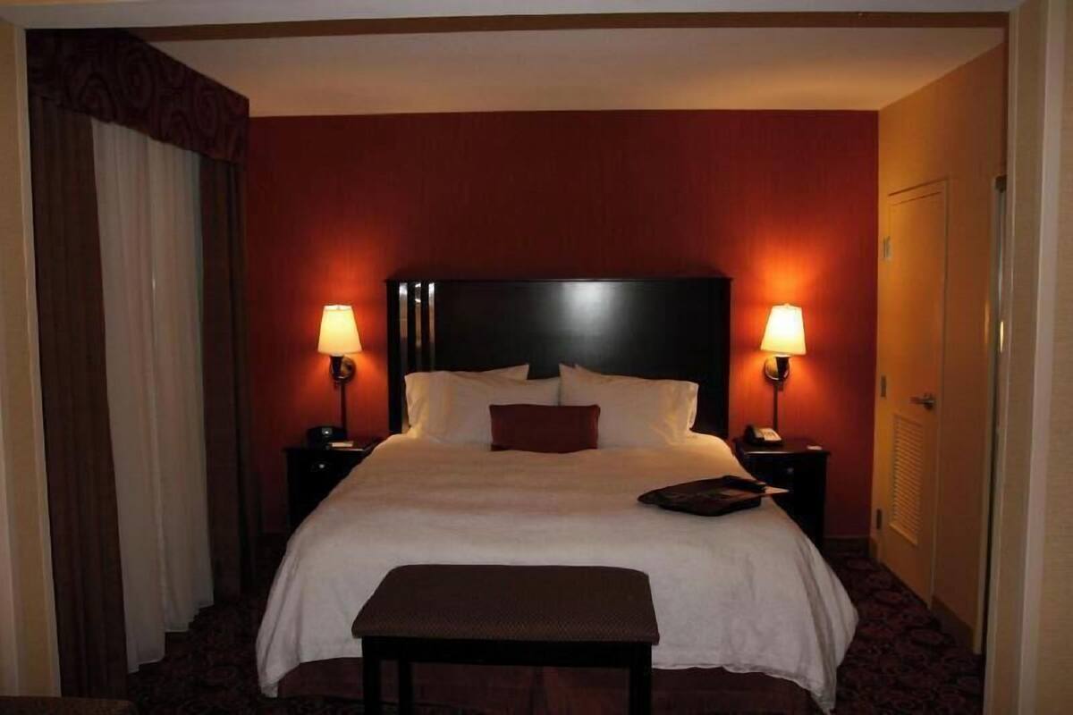 A hotel room with a large bed, two bedside lamps, a nightstand, a door, and a window with curtains.