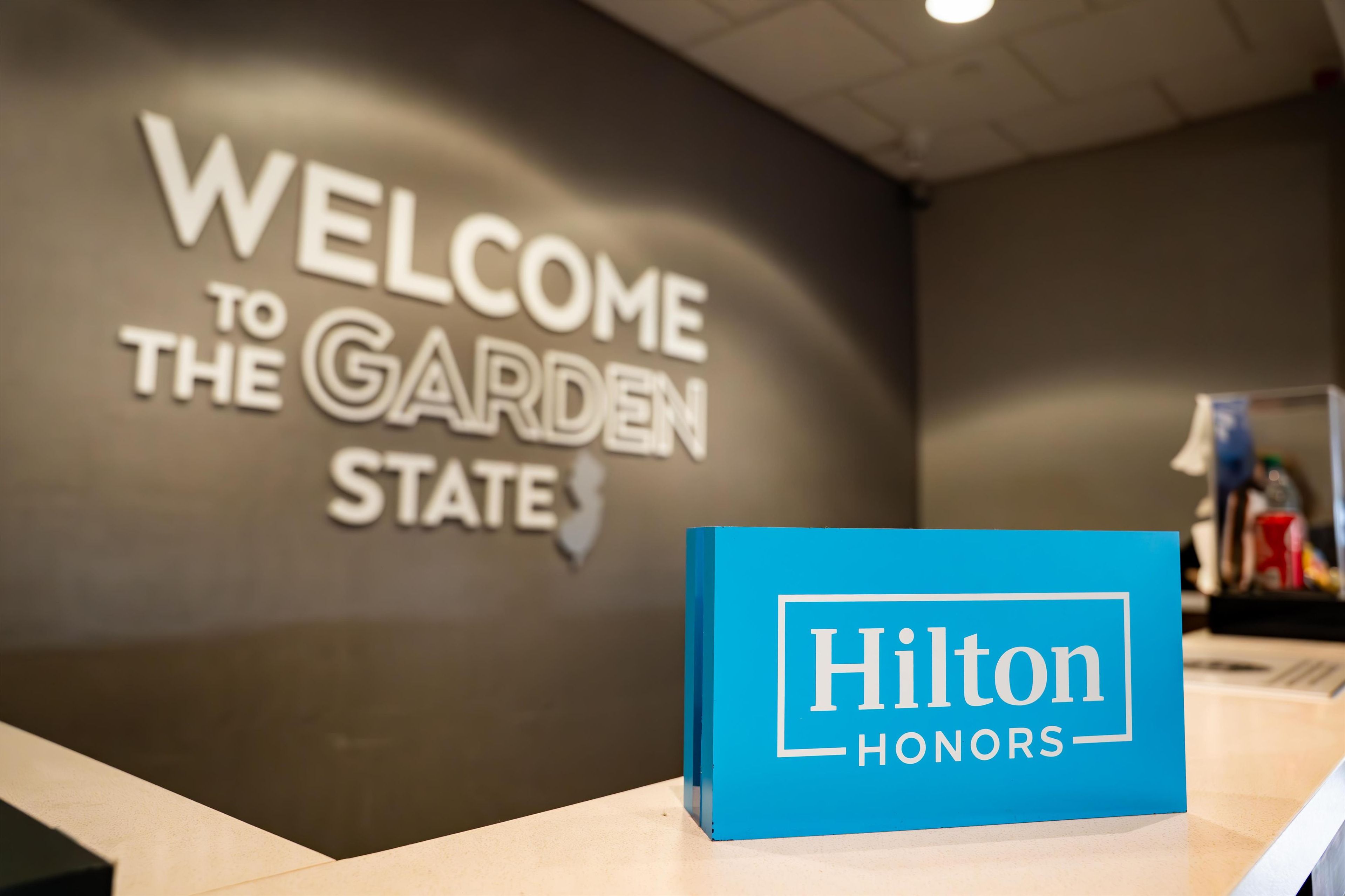 Un mostrador de recepción con un cartel que dice "WELCOME TO THE GARDEN STATE" y un letrero azul de "Hilton Honors".