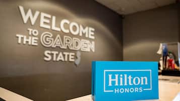 Un taulell de recepció amb un cartell que diu “WELCOME TO THE GARDEN STATE” i un rètol blau de “Hilton Honors”.