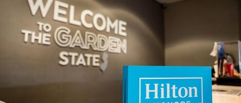Un mostrador de recepción con un cartel que dice "WELCOME TO THE GARDEN STATE" y un letrero azul de "Hilton Honors".