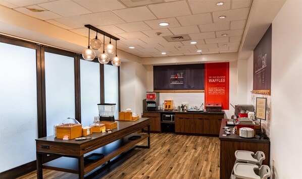 A modern kitchen with wooden flooring, a long counter, and a hanging light fixture.