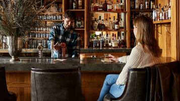A bar with wooden shelves stocked with various liquor bottles, a bar counter, and two bar stools.