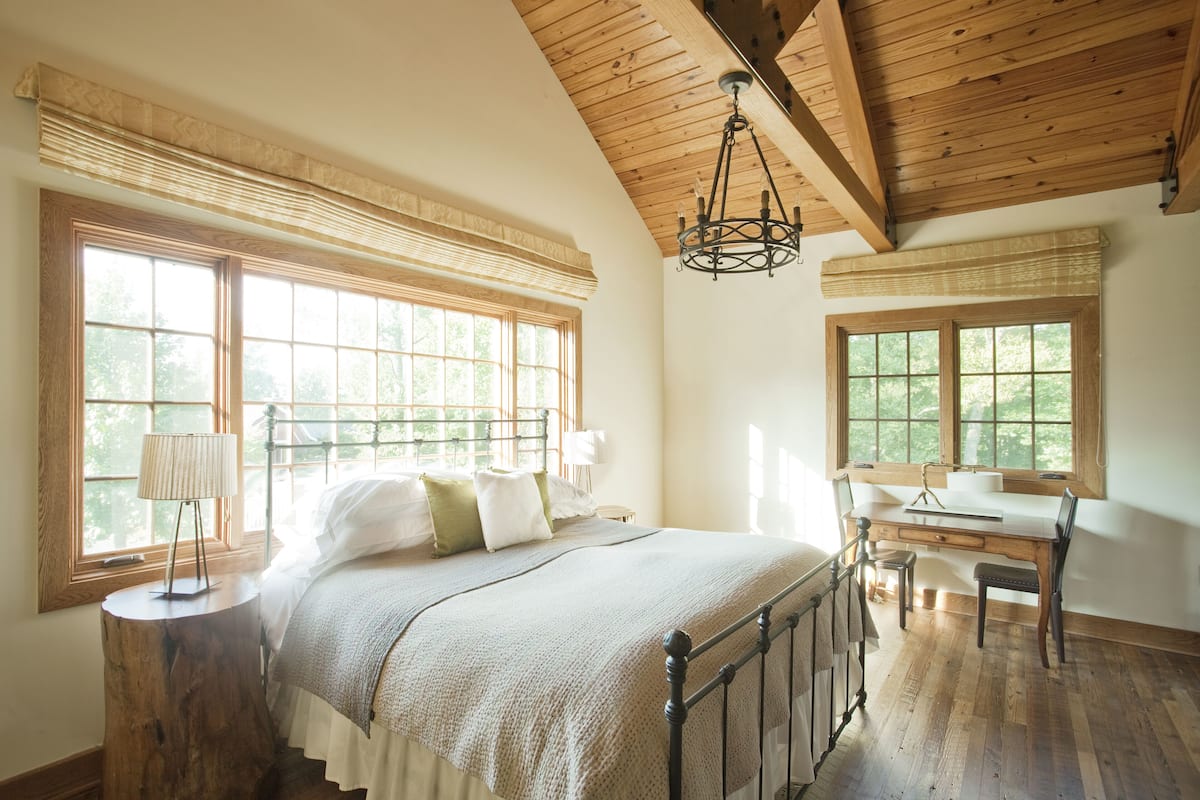 A bedroom with a large bed, wooden floor, and a desk with a chair.