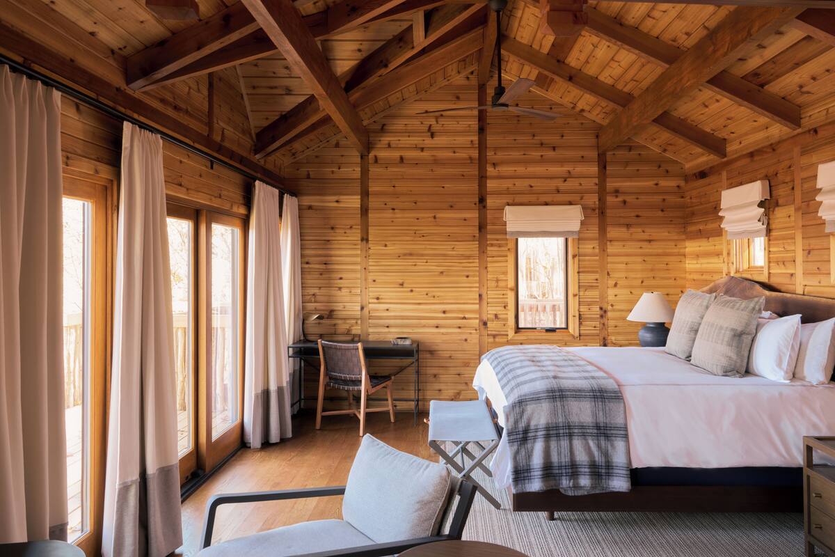 A wooden cabin room with a bed, desk, and chair.