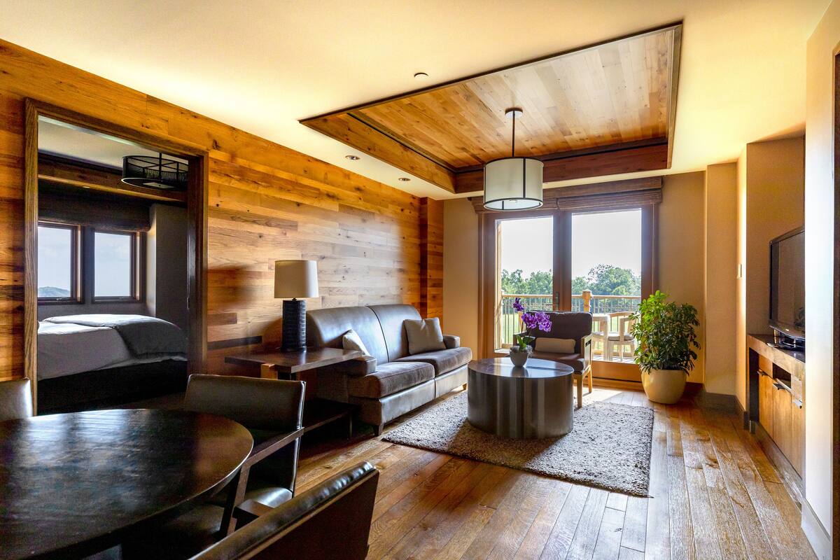 A modern living room with a wooden ceiling, a sofa, a dining table, and a TV.