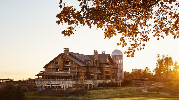 A large, multi-story wooden building with a prominent dome and multiple balconies, surrounded by a well-maintained lawn and a golf course. - The Lodge at Primland, Auberge Collection (Meadows Of Dan)