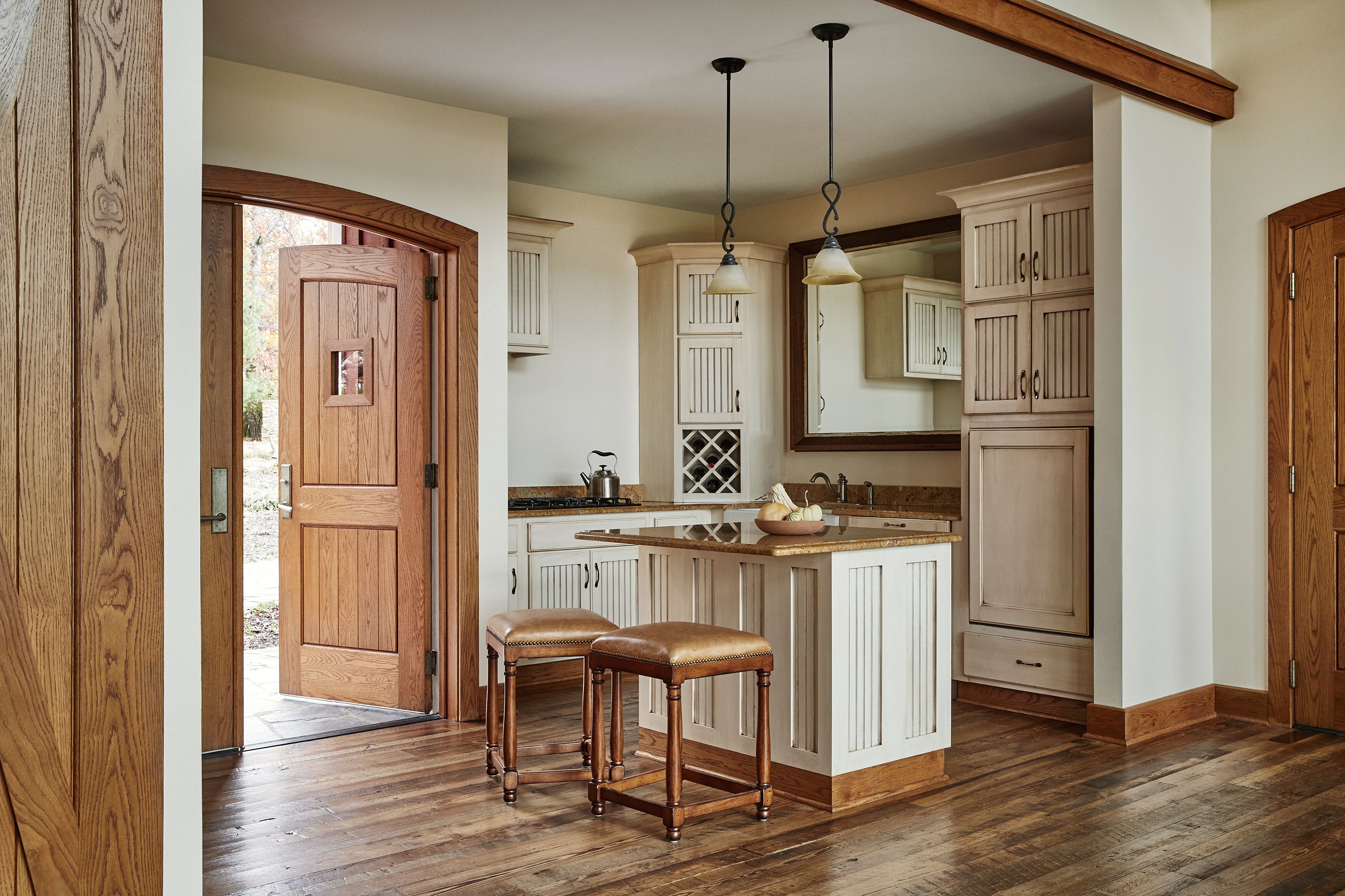 A kitchen with wooden cabinets, a central island with stools, pendant lighting, and a door leading outside.