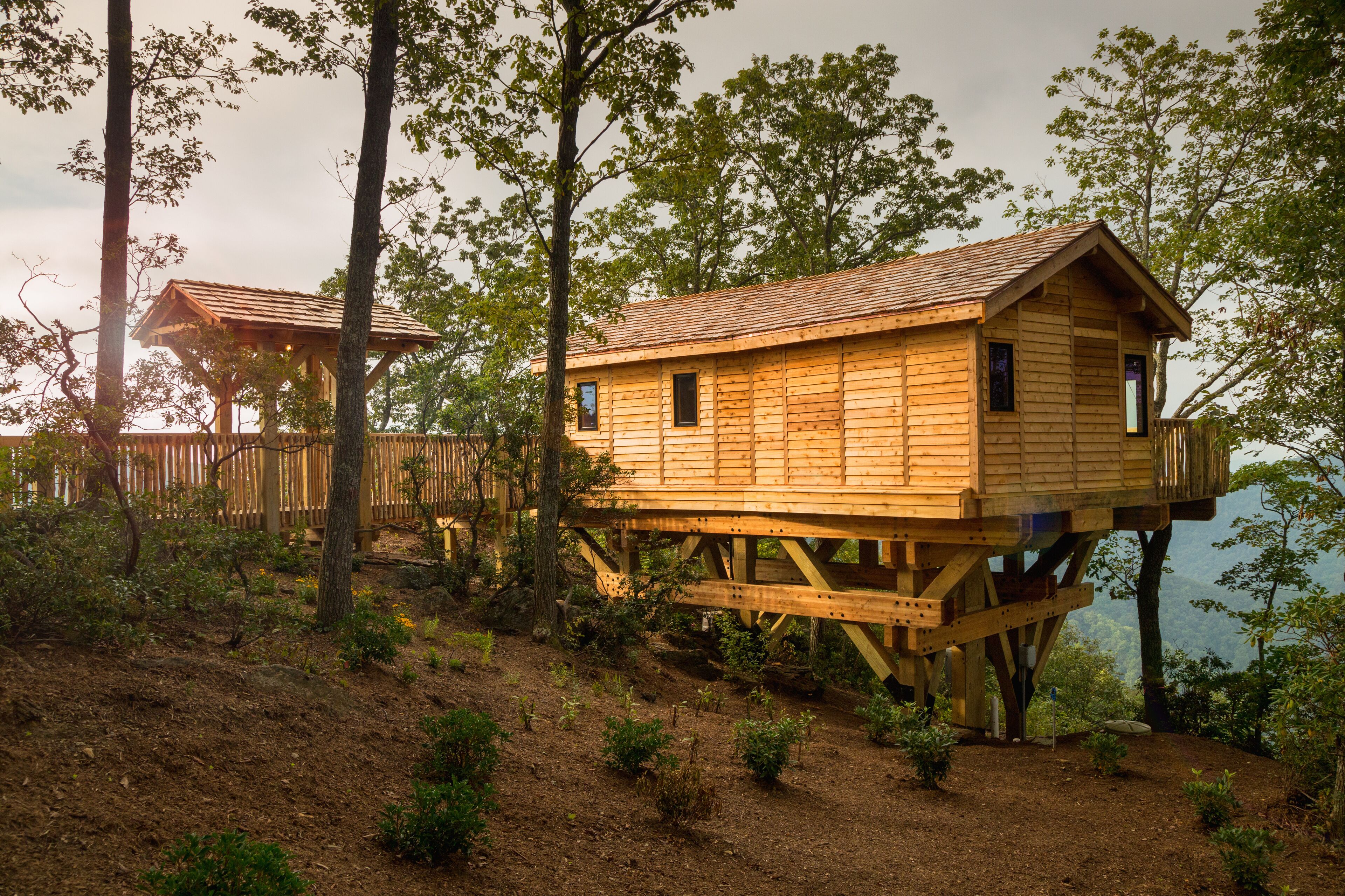 Una casa en el árbol de madera con balcón, rodeada de árboles y un paisaje natural.