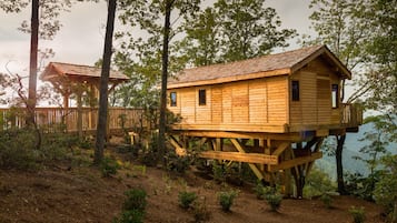 Una casa en el árbol de madera con balcón, rodeada de árboles y un paisaje natural.
